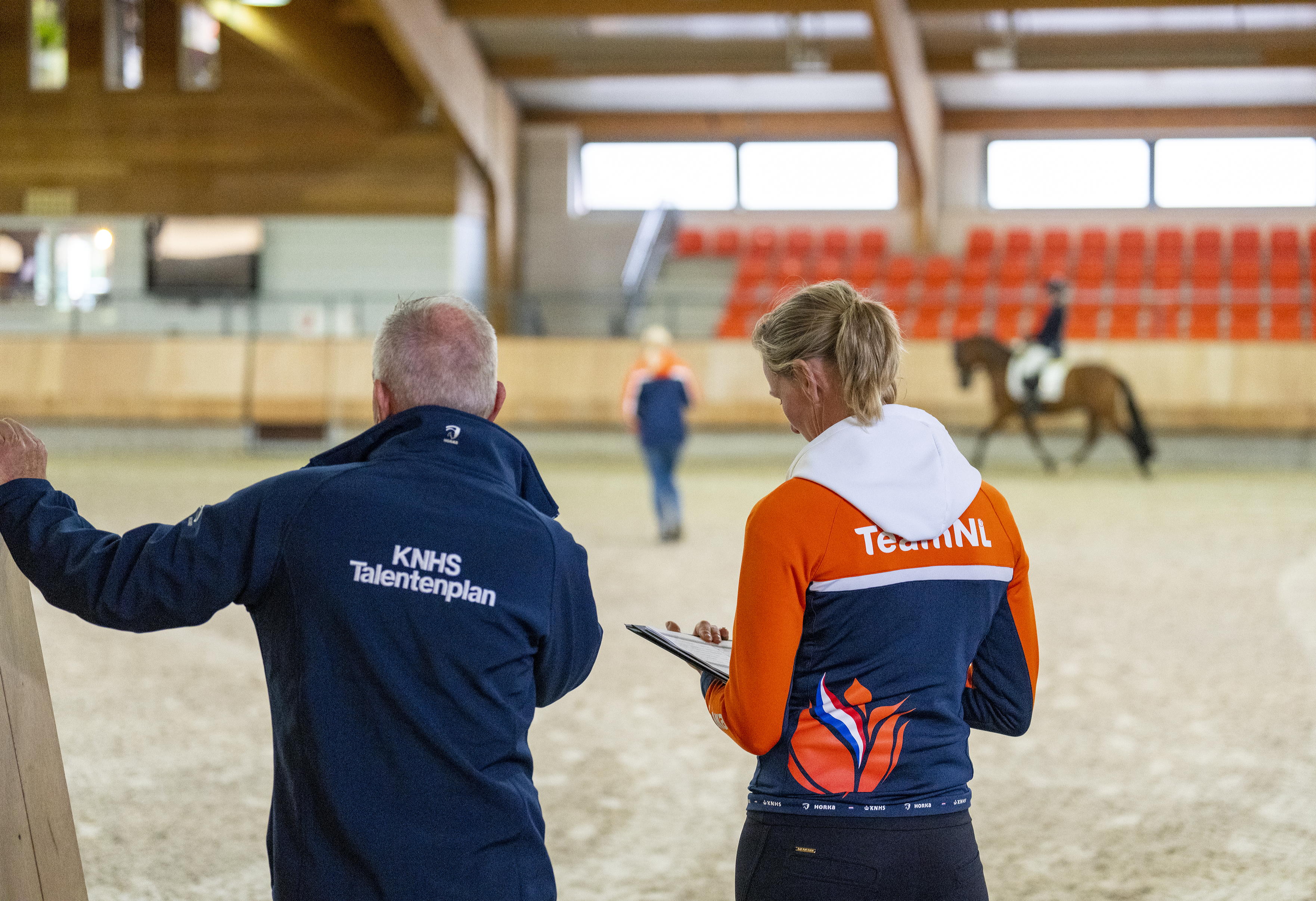 Twee trainers beoordelen een ruiter in de rijbaan